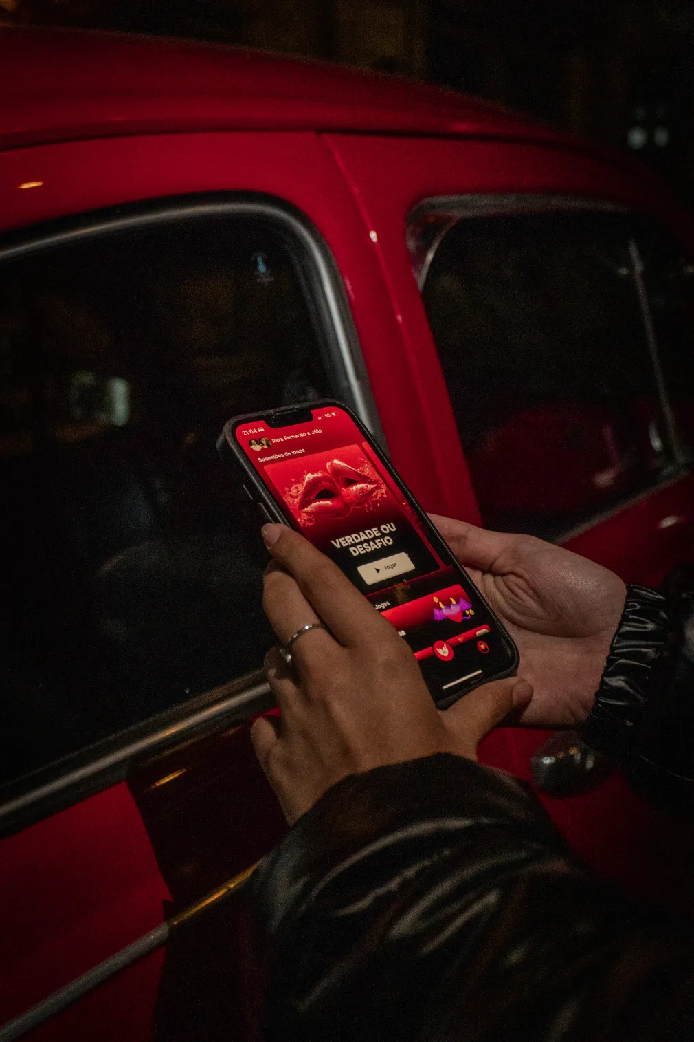 Mão segurando o celular com o Heat aberto, ao lado de um carro vermelho à noite